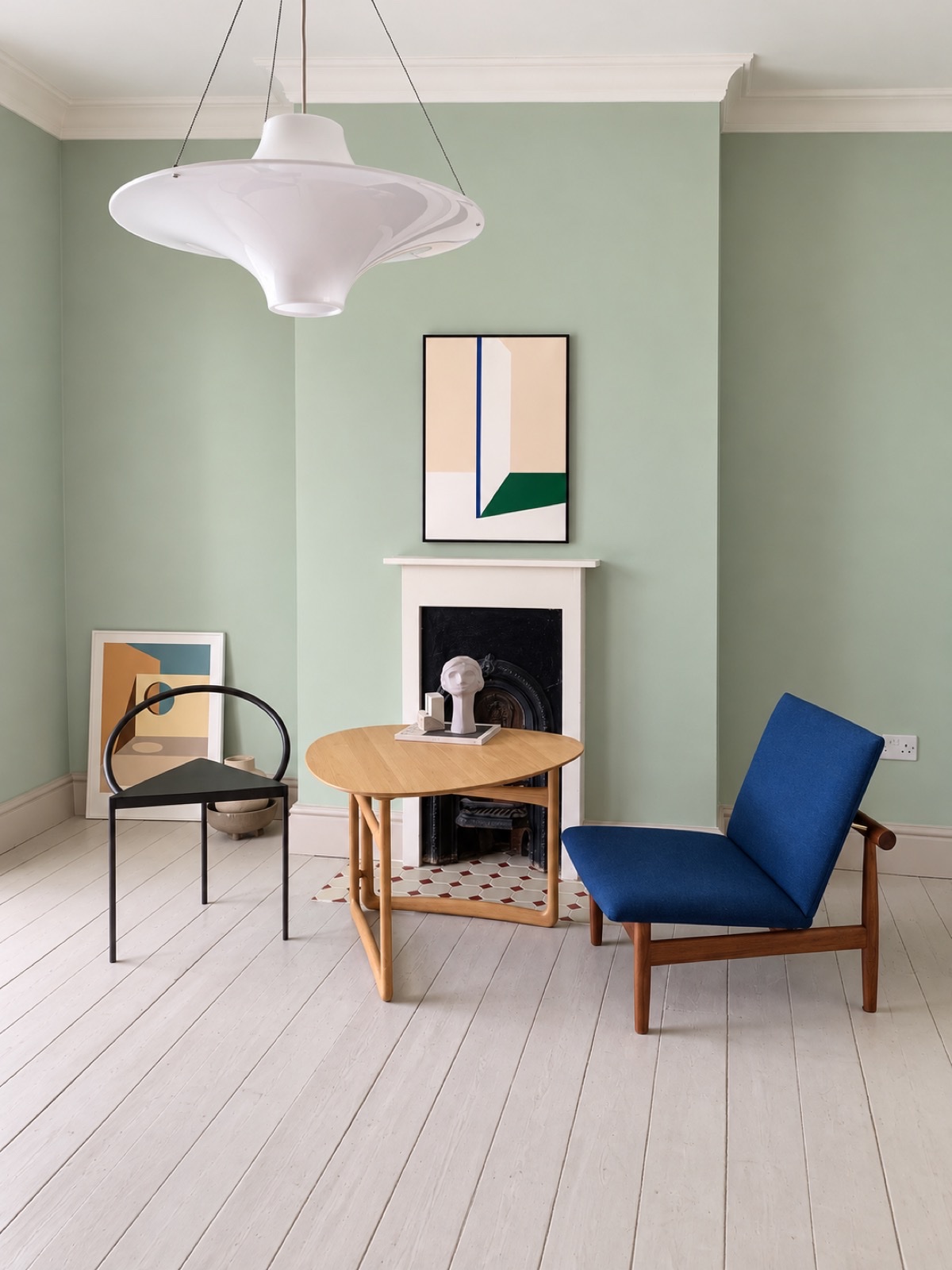 Living room with a soft green wall, a round oak table and a blue lounge chair